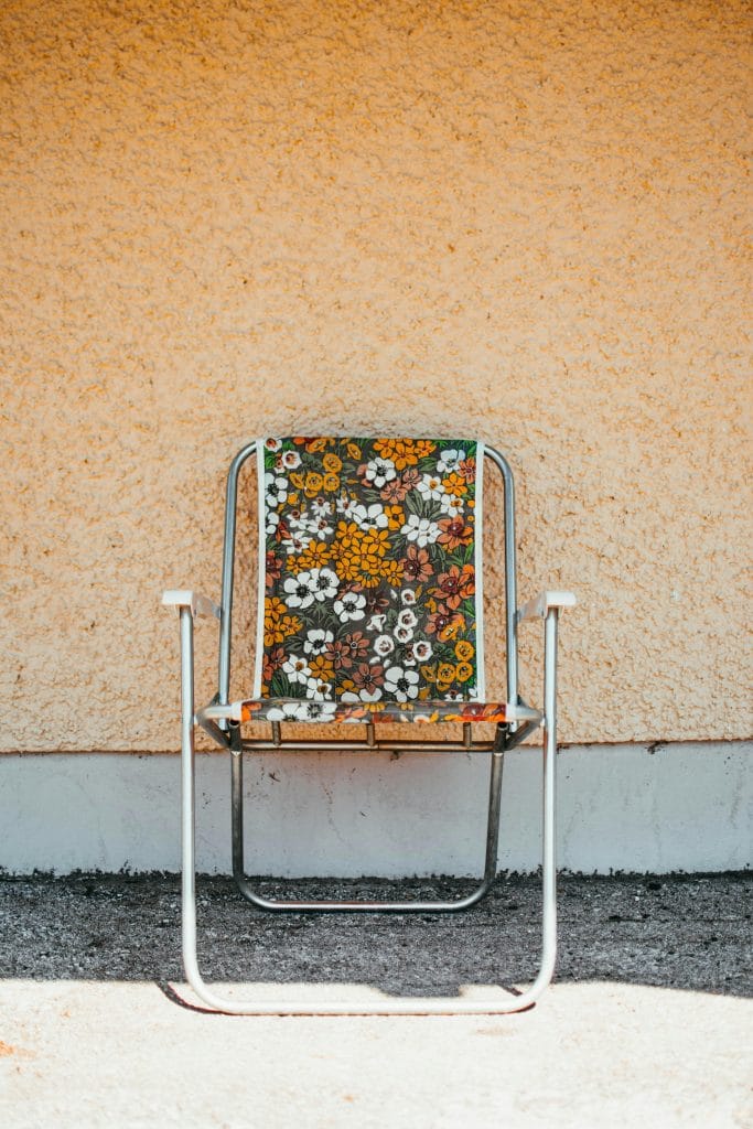 An empty vintage chair with vibrant floral patterns set against a textured wall, capturing retro style.